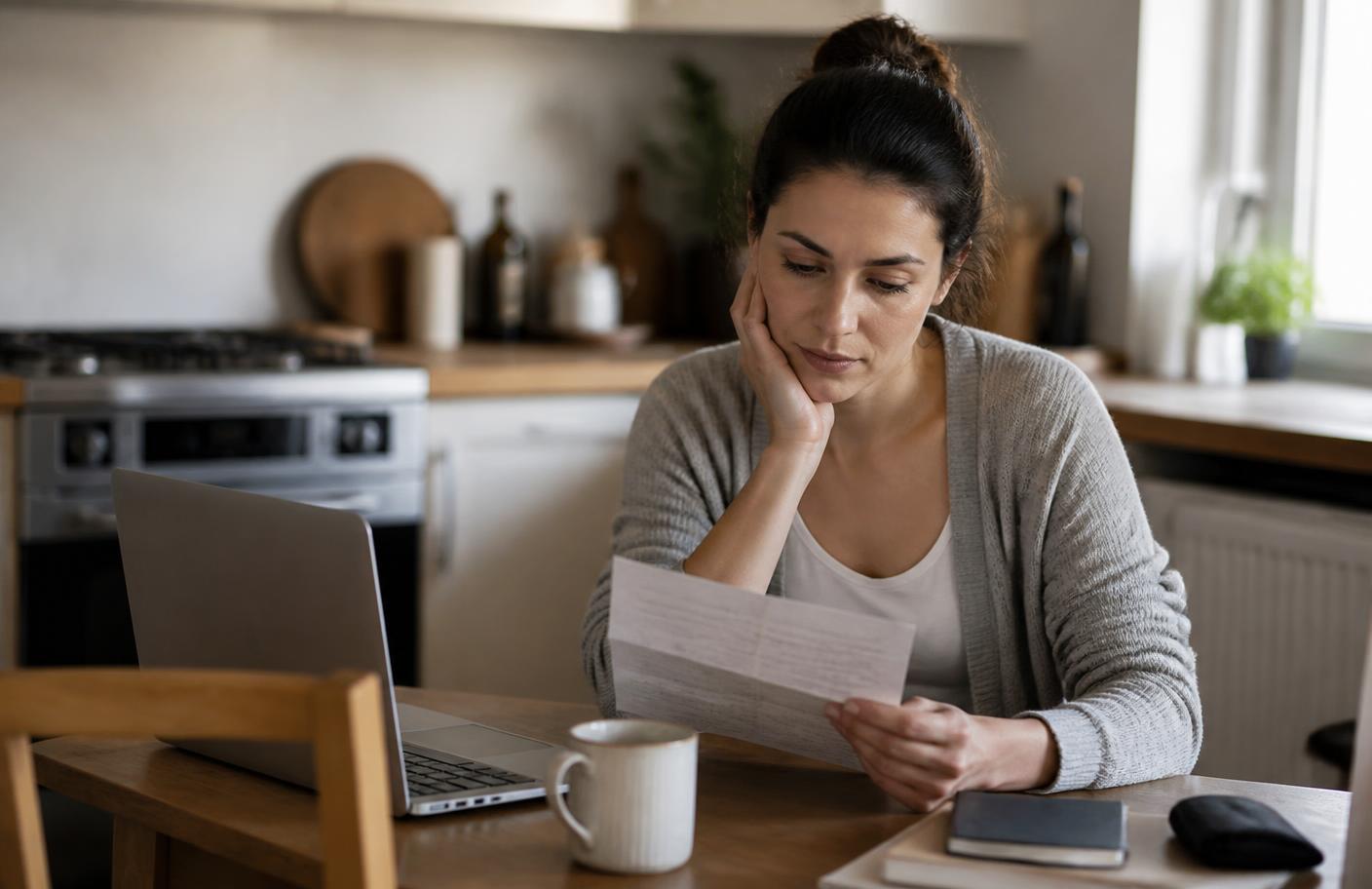 A consumer reading a response letter at home beside a laptop